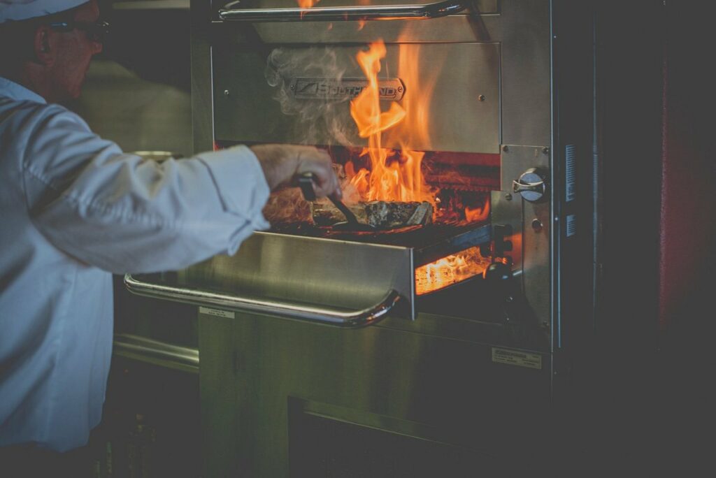 Cocinero manipula una pieza de carne en un horno profesional Southbend a altas temperaturas con fuego vivo.