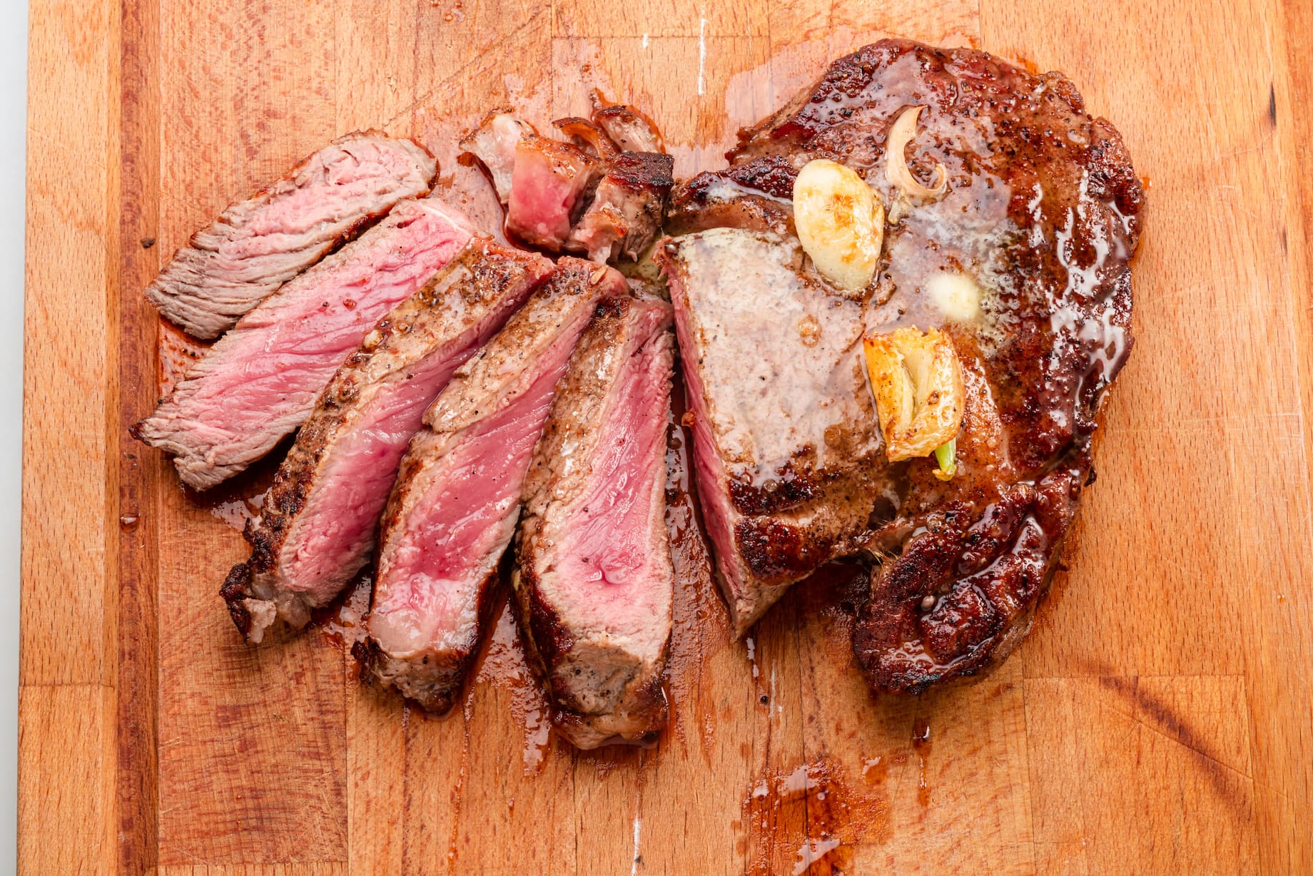 Chuletón de ternera al punto cortado en lonchas sobre una tabla de madera, con ajo y jugos de cocción.