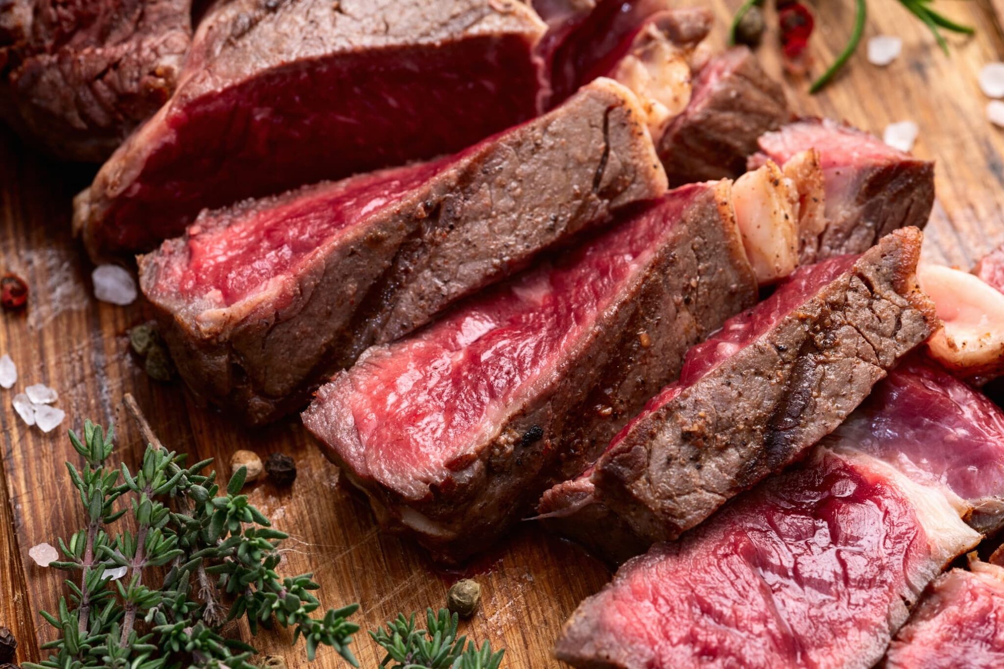 Carne de ternera poco hecha cortada en lonchas sobre una tabla de madera, con sal gruesa, pimienta y hierbas aromáticas.