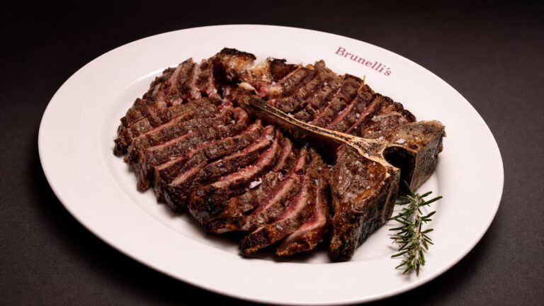 Corte de Ribeye de carne Black Angus USA trinchado en tiras y servido en plato blanco con una rama de romero.