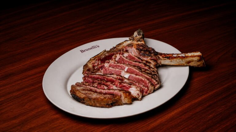 Pieza de carne Tomahawk Steak a la parrilla trinchada y servida en plato blanco.